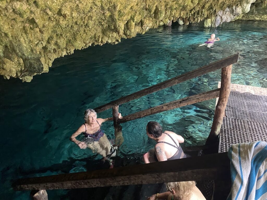 Woman smiling at cenote with swimmer in background Riviera Maya experience