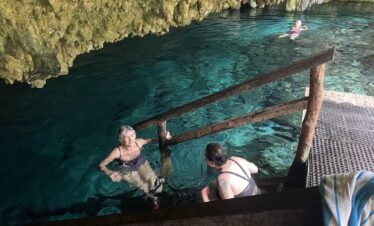 Woman smiling at cenote with swimmer in background Riviera Maya experience